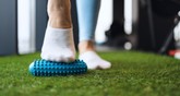 Stopa w białej skarpetce oparta o matę fitness z wypustkami na zielonej sztucznej trawie