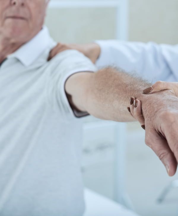 Fizjoterapeuta trzyma wyciągnięta rękę pacjenta, sprawdzając ruchomość stawu.