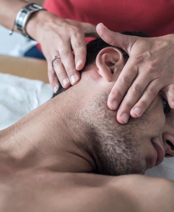 Fizjoterapeuta delikatnie rozciąga mięśnie szyi mężczyzny leżącego na wznak.